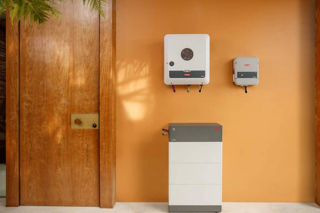 AAB Energy Solar Perth - A solar inverter, an electrical unit, and a battery storage system are installed on and against a smooth orange wall next to a wooden door.