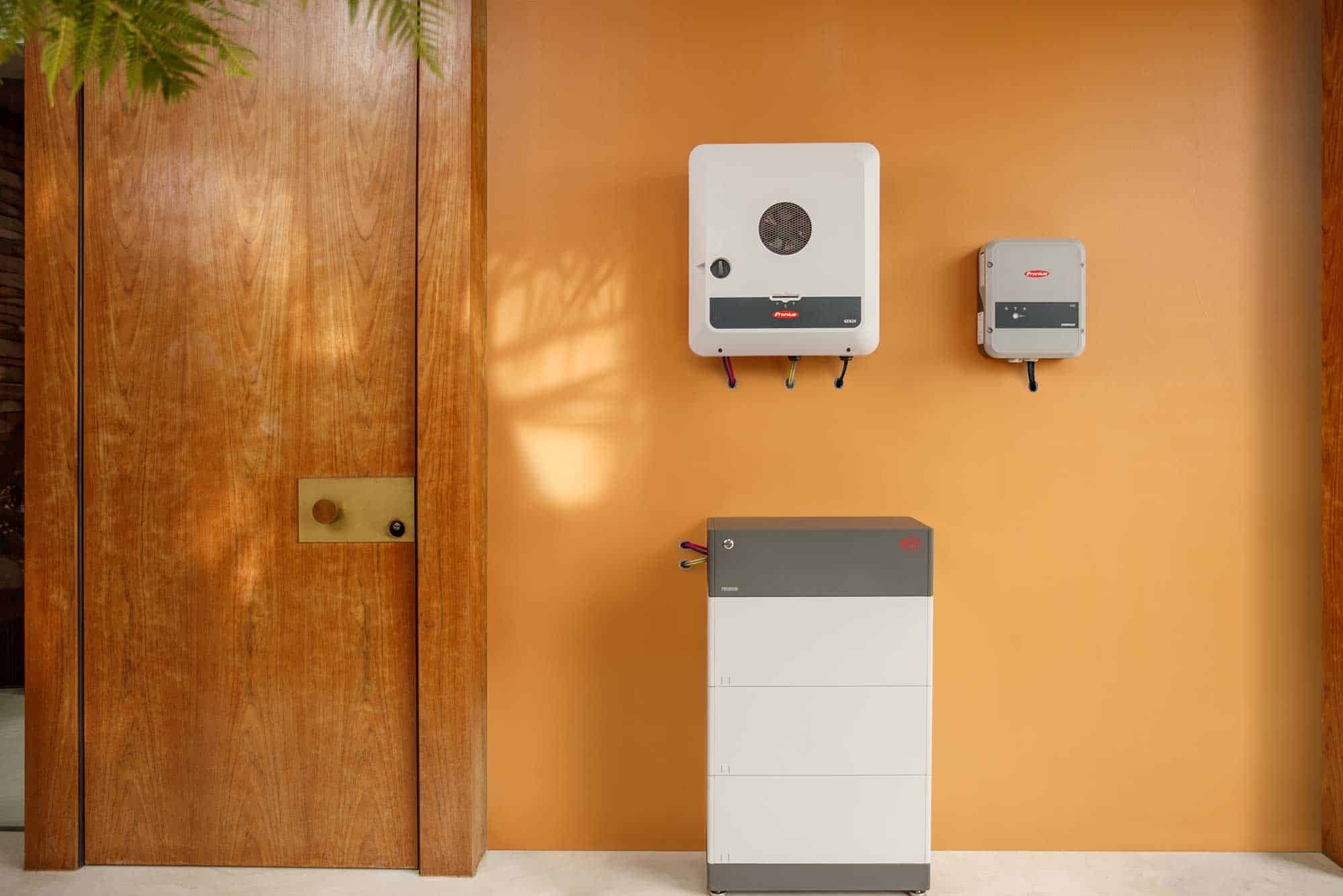 AAB Energy Solar Perth - A solar inverter, an electrical unit, and a battery storage system are installed on and against a smooth orange wall next to a wooden door.